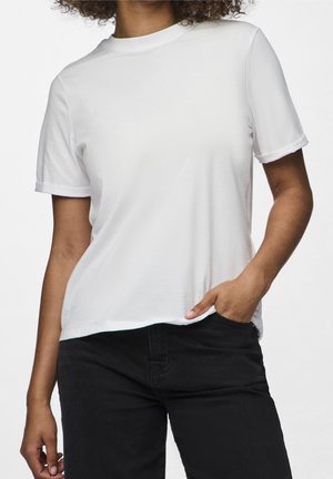 Person wearing a plain white short-sleeve t-shirt and black pants, with one hand in the front pocket.