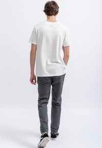 Witte t-shirt met korte mouwen en ronde hals, gecombineerd met grijze broek met elastische boorden en zwarte sneakers met witte zolen.
