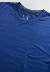 T-shirt de sport bleu de taille moyenne de Next Active avec un motif texturé en vagues et un col rond.