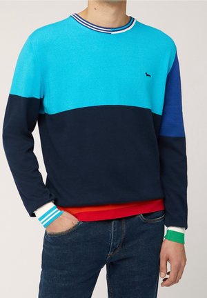 Sudadera bicolor con secciones en turquesa, marino y azul, y un cuello acanalado. Los acentos incluyen puños a rayas en blanco, turquesa y verde.