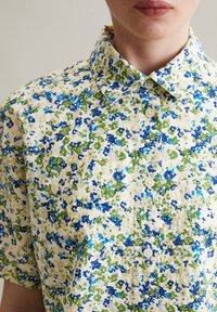 Kurzärmliges Hemd mit Knöpfen in Creme mit floralem Muster in Blau und Grün. Weicher Stoff mit klassischem Kragen und zwei Knopfverschlüssen.