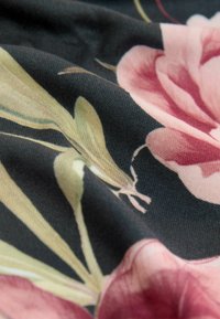 Květinová látka s růžovými a krémovými květy na tmavém pozadí; měkká textura s propracovanými barevnými vzory a detaily na listech.