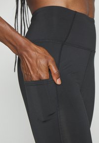 Svarta tights gjorda av ett elastiskt material med en sidoficka. Har platta sömmar och en hög midja för en säker passform.