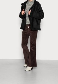 Zwarte nepbont gevoerde jas, grijze gebreide trui, bruine corduroy flare pants met witte knopen, en witte enkellaarsjes met zwarte accenten.