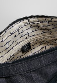 Primo piano di una borsa blu con zip aperta che mostra un rivestimento in tessuto crema con testo in corsivo nero e un'etichetta del marchio Kipling all'interno.
