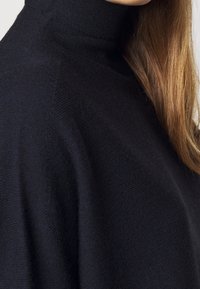 Granatowy sweter dziany z wysokim kołnierzem, wykonany z teksturowanej tkaniny o luźnym kroju, podkreślający miękki, lekko prążkowany wzór.