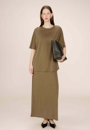 T-shirt marron surdimensionné et jupe maxi assortie en tissu doux. Pochette noire à la main et chaussures noires à bout pointu. Design simple.