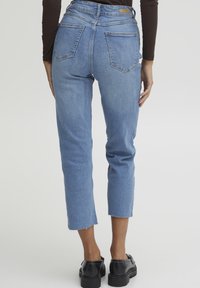 Jeans de mezclilla azul con cintura alta, largo recortado y dobladillo sin rematar. Cuenta con dos bolsillos traseros y una textura suave.