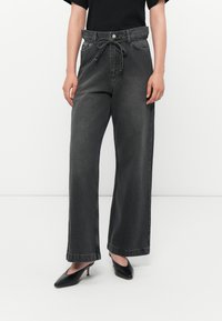 Grå denim vid ben bukser med taljebånd, med frontlommer og lige snit. Bæres med sorte hæle mules.