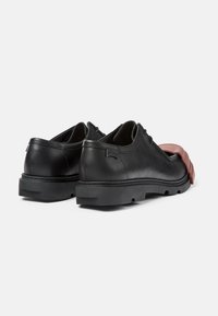 Zapatos de cuero negros con puntera redonda, suela de goma y acentos rojos en la parte delantera, con textura suave y diseño minimalista.