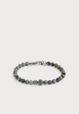 Bracelet avec des perles rondes gris-vert et une perle décorative centrale en argent avec un motif floral et une fermeture à clip sur fond blanc.