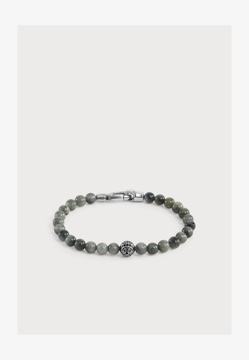 Bracelet avec des perles rondes gris-vert et une perle décorative centrale en argent avec un motif floral et une fermeture à clip sur fond blanc.