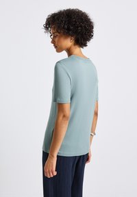 Měkké, světle modré tričko s krátkým rukávem a kulatým výstřihem. Tkanina je hladká, s postranními rozparky na lemu. Nenošené s námořnickými kalhotami s texturou.