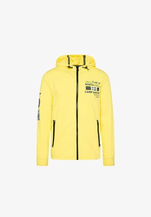 Żółta kurtka z kapturem wykonana z materiału z czarnymi suwakami. Posiada nadrukowany tekst i grafikę na klatce piersiowej i rękawie, a także boczne kieszenie.