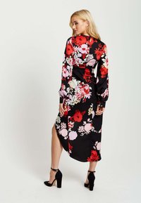 Floral dress featuring a black background with vibrant red and pink flowers, long sleeves, a side slit, and buttoned cuffs.