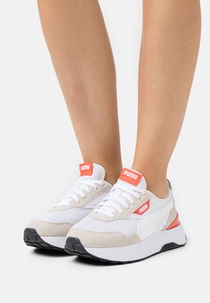 Białe i beżowe buty sportowe wykonane z siateczki i zamszu, z czerwonymi akcentami i sznurówkami oraz czarną gumową podeszwą.