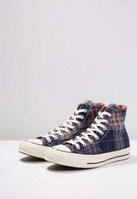 Hochwärtige Sneakers aus dunkelblauem karierter Leinwand mit beigen Akzenten, weißen Gummisohlen und kontrastierenden Nähten. Runde Zehenform und Schnürdesign.