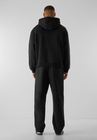 Ensemble composé d'un hoodie noir et d'un pantalon de survêtement, fabriqué dans un matériau doux, doté d'une capuche spacieuse, de poignets côtelés et d'une coupe décontractée.