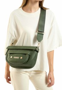 Olijfgroene leren schoudertas met een voorflap, ritsluiting, twee goudkleurige studs en een brede verstelbare band. Glad oppervlak.