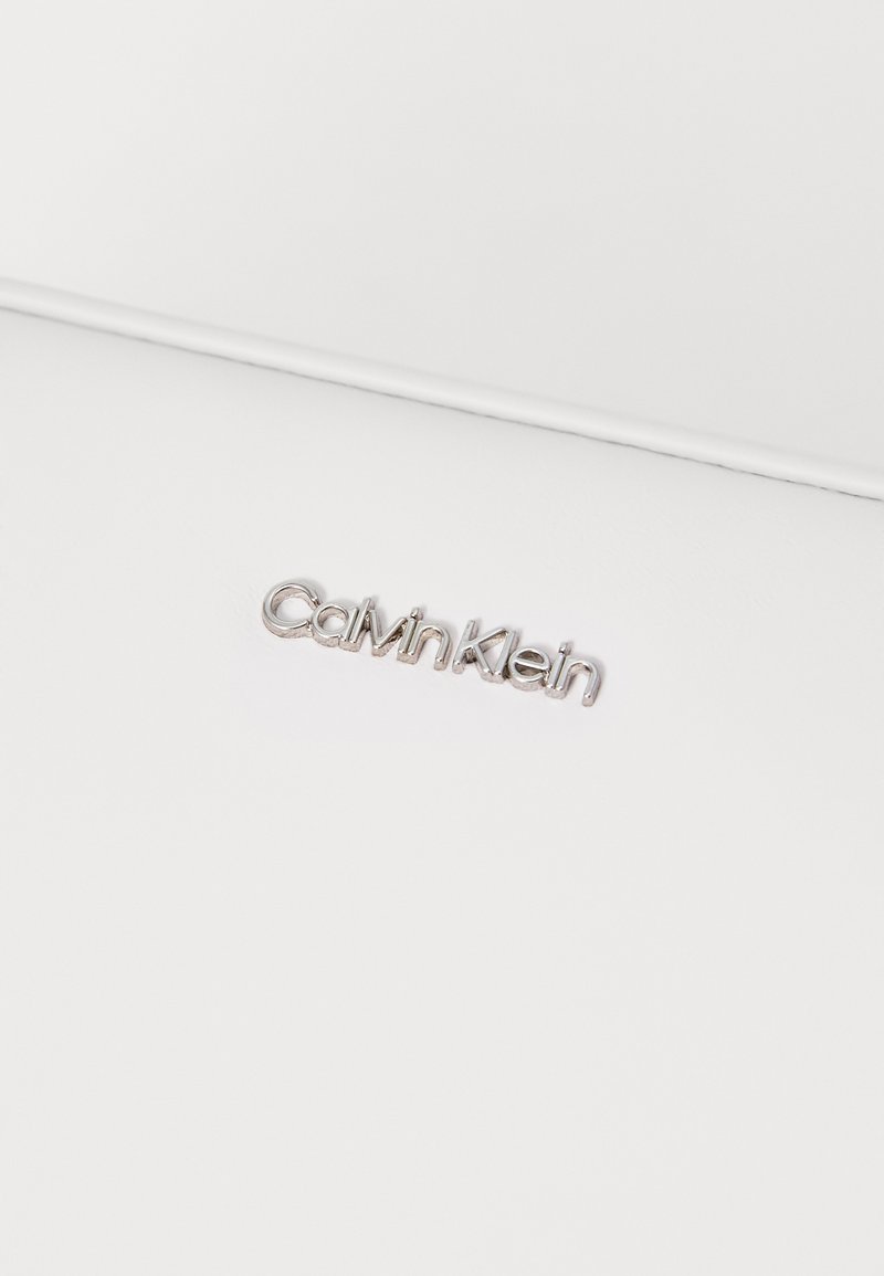 Logo argento di Calvin Klein su uno sfondo bianco texturizzato, caratterizzato da un design elegante e minimalista con linee pulite.