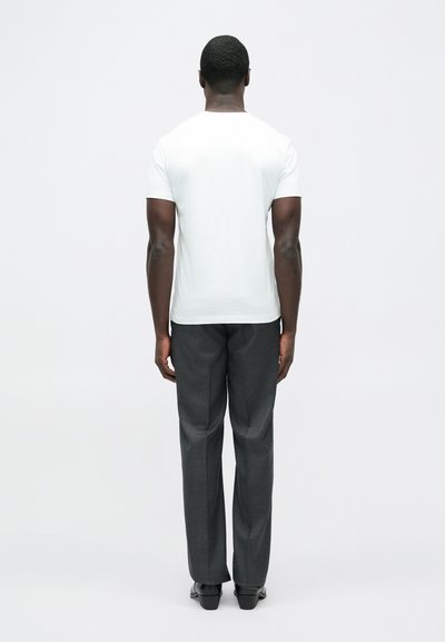 Hvid t-shirt med korte ærmer kombineret med grå skræddersyede bukser. Stoffet ser glat ud; bukserne har et diskret mønster og en lige pasform.