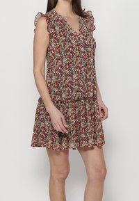 Robe fleurie avec une base rouge ornée de fleurs vertes et jaunes, manches courtes à volants, devant boutonné et ourlet à volants à étages.