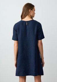 Navyblaue Leinenkleid mit kurzen Ärmeln, lockerer Passform und einem Rundhalsausschnitt, der auf der Rückseite ein Schlüssellochdetail aufweist. Glatte Textur.