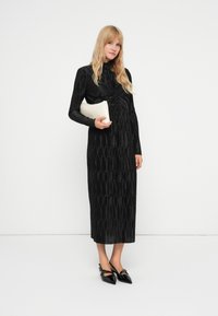 Fekete bordázott, hosszú ujjú ruha csomózott derékrésszel, amit egy krémszínű táskával és fekete hegyes orrú magassarkúval párosítottak. Az egész sima tapintású.