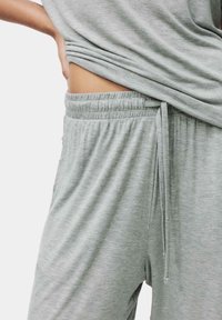 Lys grå loungewear sæt med en løstsiddende top og bukser med elastisk talje og snor, lavet af blødt, struktureret stof.