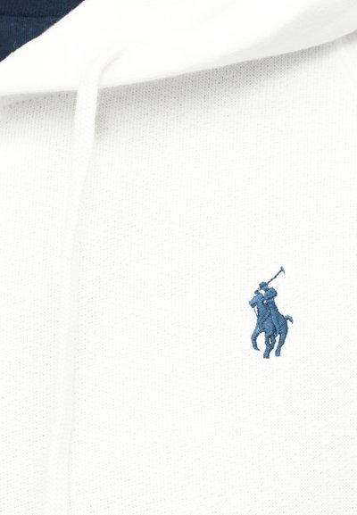 Sweat à capuche blanc avec un logo brodé bleu marine représentant un joueur de polo à cheval tenant un maillet levé, situé sur la poitrine.