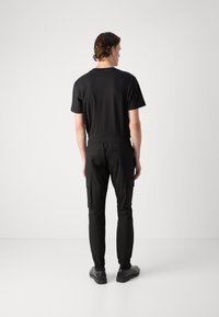 Tricou din bumbac negru cu mâneci scurte, asortat cu pantaloni cargo negri cu talie elastică și buzunare laterale, purtati cu pantofi negri.