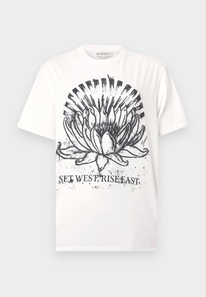 T-shirt blanc avec motif graphique de fleur abstraite noire et texte « SET WEST, RISE EAST » imprimé sous le design à l'avant.