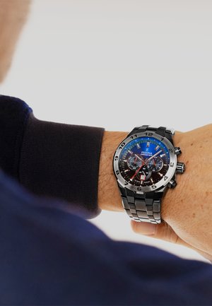 Montre chronographe argent et noir avec un cadran dégradé bleu, des accents en acier inoxydable et un bracelet en métal à motifs.
