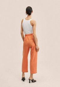 Orange linen wide-leg pants with an elastic waistband and back pockets, paired with a white tank top and black heeled sandals.