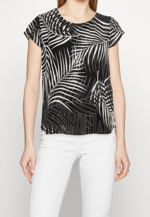 Top de patrón de hojas tropicales en blanco y negro, con mangas cortas, escote redondo, tejido ligero y corte relajado, combinado con pantalones blancos.