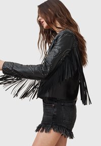 Juoda odinė striukė su kutais ir sidabriniais smeigtukais. Striukė aptemptos silueto, ilgomis rankovėmis ir trumpintu kraštu.