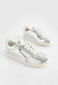 Sneakers bianchi con una finitura metallica lucida, caratterizzati da un design elegante, chiusura con lacci, dettagli per perforazione e suola in gomma testurizzata.