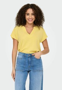 Geel kort mouwtopje met een V-halsontwerp, gemaakt van lichtgewicht stof. Gepaard met hooggetailleerde lichtblauwe denim jeans.