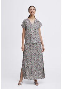 Ensemble fluide composé de deux pièces avec un motif floral vert, rose et violet, doté d'un décolleté en V et de fentes sur la jupe. Sandales argentées.