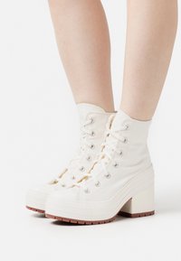 Weiße High-Top-Stiefel aus Canvas mit strukturiertem Absatz, runder Zehenpartie und Gummisohle. Mit Schnürung vorne und metallischen Ösen.