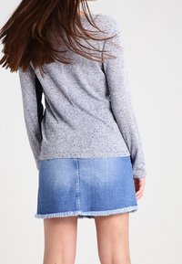 Graues Langarmoberteil kombiniert mit einem hellblauen Jeans-Minirock mit ausgefranstem Saum. Der Stoff wirkt weich mit einer strukturierten Oberfläche.