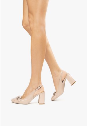 Scarpe con tacco alto type slingback in pelle sintetica lucida beige, caratterizzate da un accento a fiocco e un tacco squadrato spesso. Texture liscia e design raffinato.