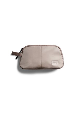 Petite pochette rectangulaire beige avec fermeture éclair, tirette en tissu et étiquette de marque sur le devant, conçue pour transporter des objets personnels.