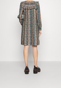 Šaty s květinovým vzorem v tmavě modrozelené barvě, s volánkovým límcem a dlouhými rukávy, s výstřihem na zádech a volným střihem. Černé chunky boty.