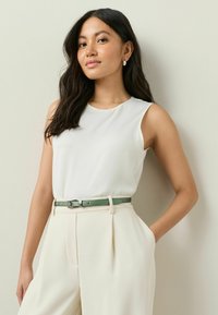 Hvid ærmeløs top parret med cremefarvede bukser og et grønt bælte. Glat stof med et minimalistisk design, der fremhæver en moderne stil.