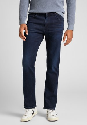 Mörkblå denimjeans med rak passform, med fem fickor och en klassisk knapp- och dragkedjestängning. Bärs med en ljusgrå tröja.