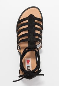 Sandale en daim noir avec de multiples brides croisées, une semelle intérieure nude et une bride à nouer à la cheville. La semelle est plate avec une forme de bout arrondi.