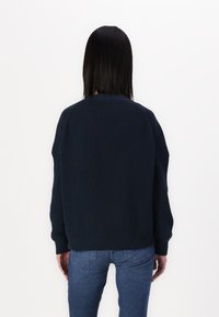 Granatowy sweter dzianinowy o prążkowanej fakturze, z szerokimi rękawami i luźnym krojem. Noszony na dżinsach, prezentujący casualowy styl.