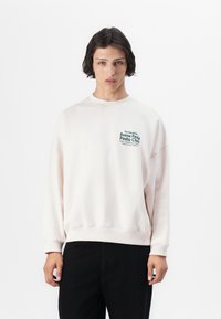 Lichtroze sweatshirt met een ronde hals en een drop shoulder design. Bevat een groene tekstprint op de borst. Gemaakt van zachte, textuurstof.