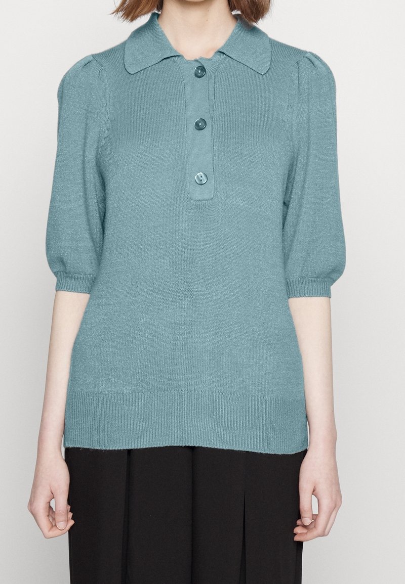 Světle modrý pulovr s krátkým rukávem, límcem, třemi knoflíky, žebrovaným lemem a manžetami a hladkým texturovaným materiálem.